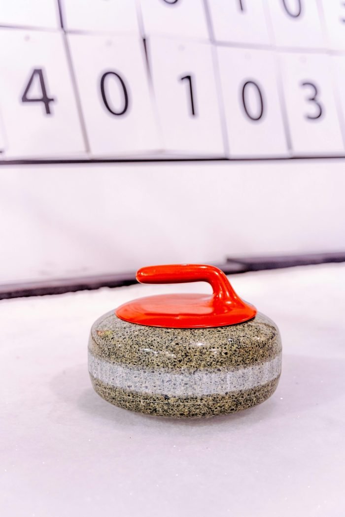 Detailed view of a curling stone on an ice rink with scoreboard in background.